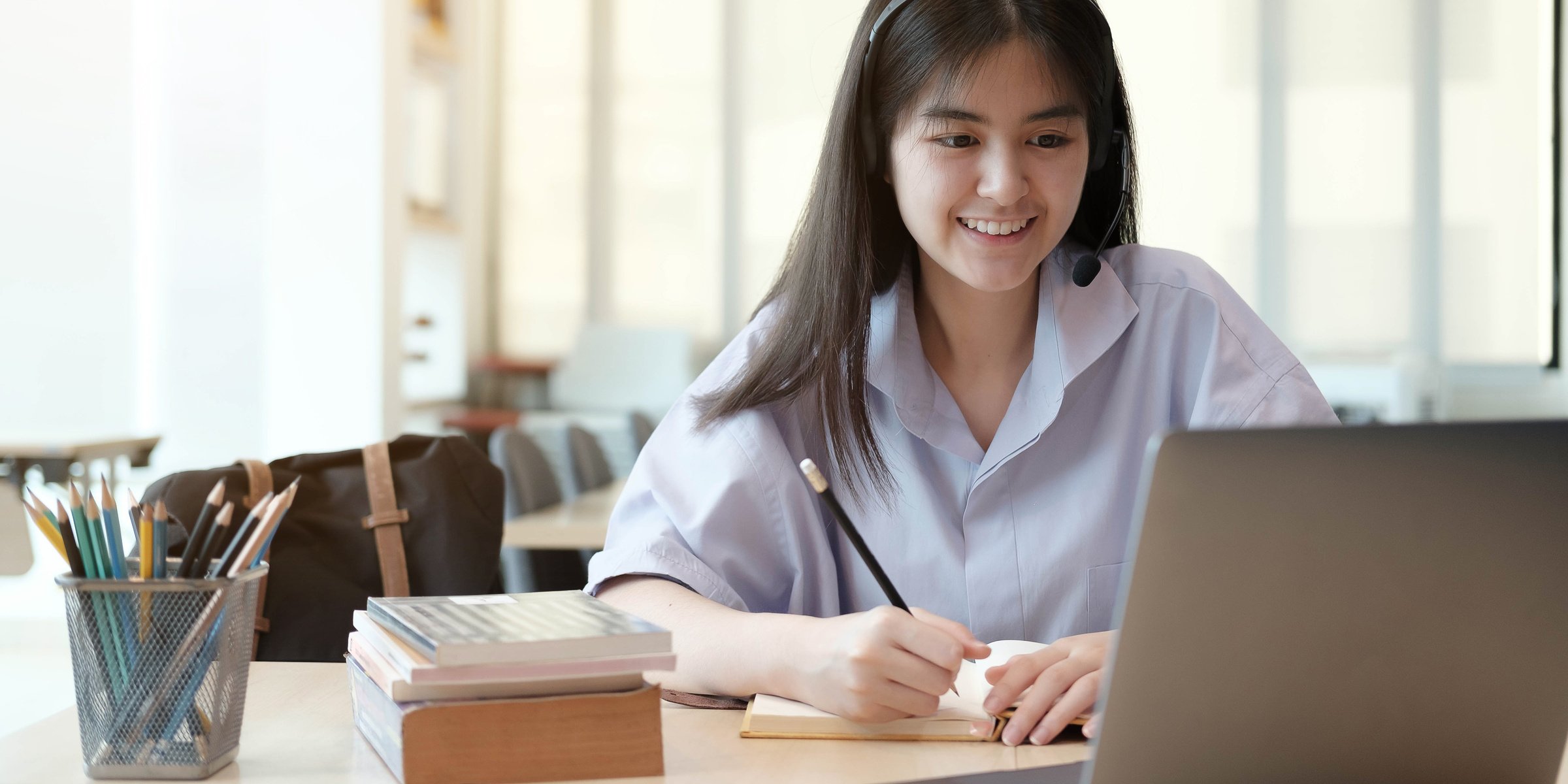 Happy Young Thai Girl with Wireless Headphones Looking at Laptop